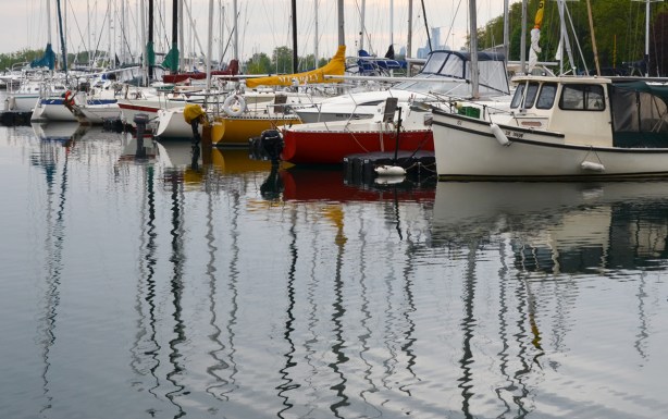 reflections of sailboats and their masts in Lake Ontario, boats are parked at a yacht club 