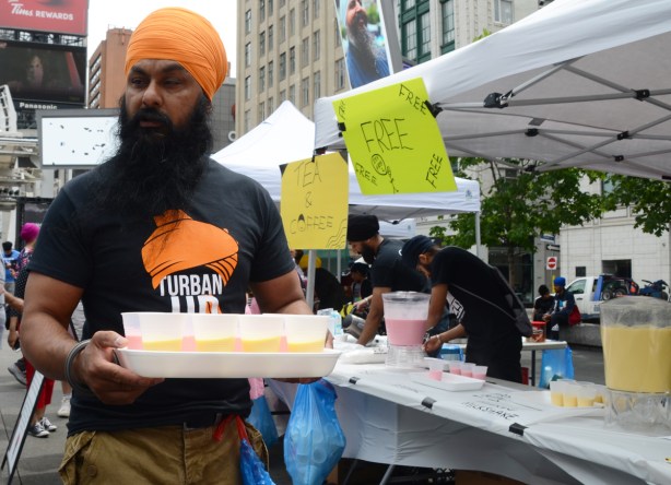 a sikh man in bears and orange turban carries a tray of cups of mango and rose milkshake