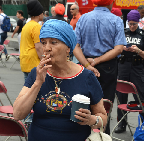 an older woman in a light blue turban smokes a cigarette