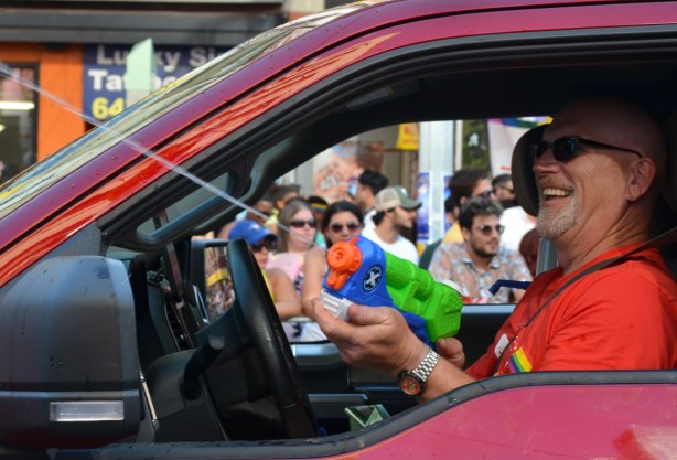 a man driving a red vehicle is spraying people out the window with a super soaker 