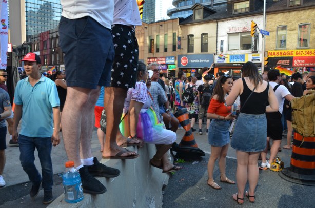 two men standing on a concrete barrier, watching parade, other people on the sidewalks