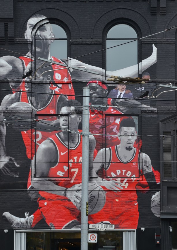 mural of the Toronto Raptors, 5 players in their red uniforms along with the coach and Drake. On a storefront on Queen Street West. 