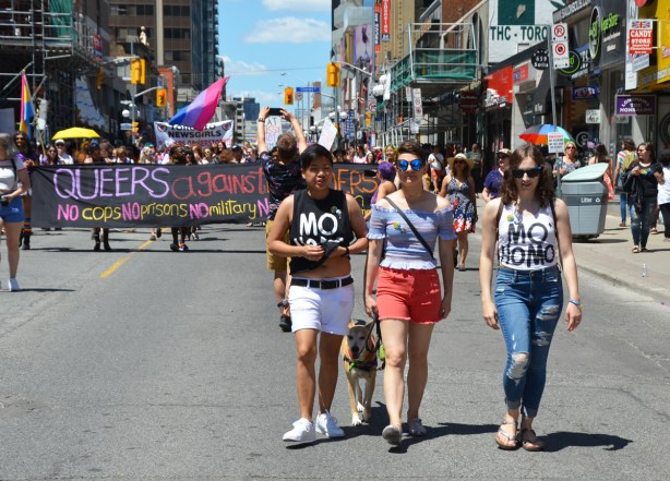 three women walking in dyke march in front of a group with a banner that says queers against borders