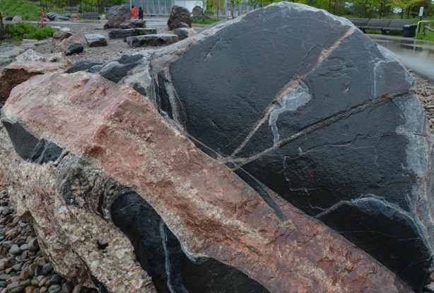 large chunk of granite in a park, black patches with streaks of pink and grey