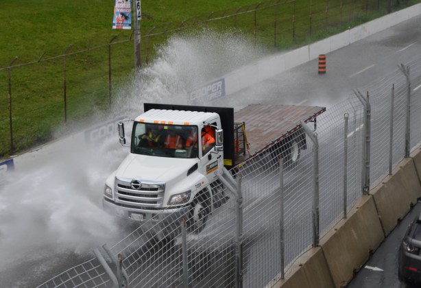 a white truck with three men in the cab on Lakeshore Blvd plows through the water and creates great splashes of water, road is partially flooded 