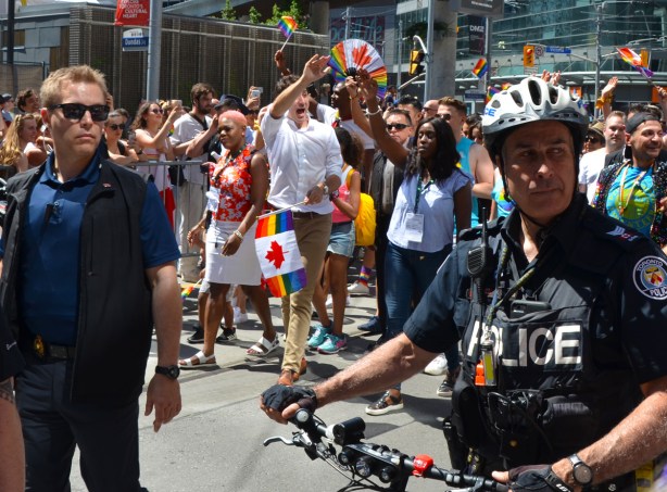 Prime Minister Justin Trudeau walks in the pride parade in Toronto with other people, waving to the crowds, police men and security detail also in the picture 