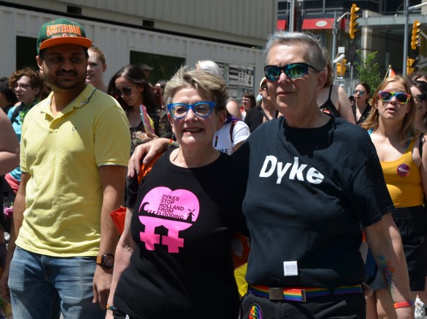 a couple walking together with black t shirts one just says dyke and the other says dykes stop Holland from flooding