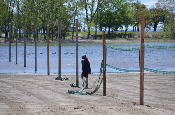 a man is putting up volleyball nets on the poles that aren't in the water at a flooded Woodbine Beach 