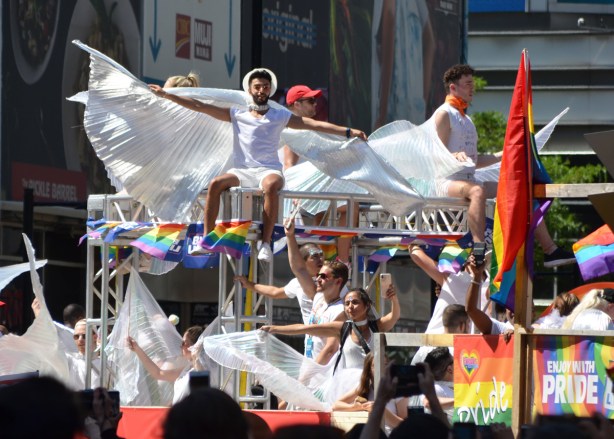 people draped in white with large white fabric wings sitting on top of a float in the pride parade 