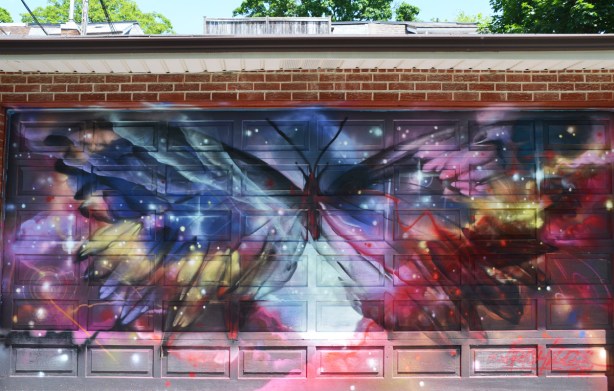 a very large butterfly on a mural on a grage door, wild colours in blues and red, It looks like the butterfly is superimposed on the whole universe 