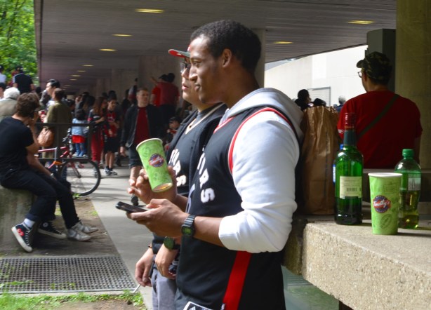Raptors fans, parade day, men leaning against a raingin beside city hall, with a wine bottle behind them