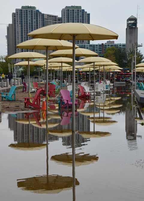 Toronto waterfront showing flooding at H 2 O park with its Muskoka chairs and yellow umbrellas, many colourful reflections in the flood waters 