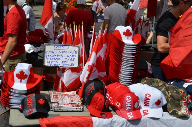 on a table outside, piles of Canada Day merchandise for sale, hats, cowboy hats, flags, etc 
