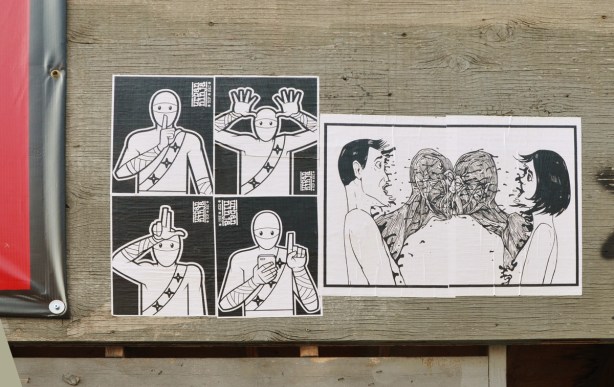 5 black and white paste ups on a wall in Kensington, four are urban ninja squadron and the the fifth is of a couple arguing, him on the left and her on the right, in the middle between them dark angry figures come nose to nose 