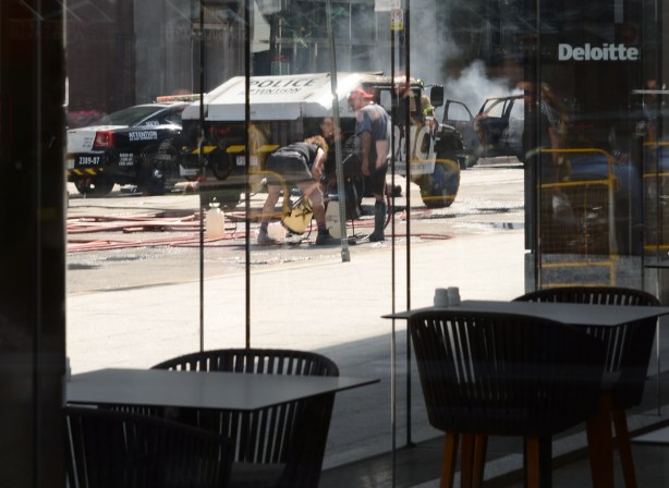 looking through the window of a restaurant with two empty tables, to a scene where a film set is setting up to shoot a scene involving exploding buses and police cars