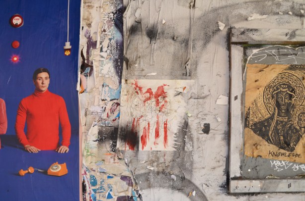 parts of a few different posters and drawings on a wall, a man in a red shirt on blue background which is part of an ad is on the left, a drawing of three naked women is in the middle (but is faint and hard to see), and a drawing on yellow labelled knowledge 