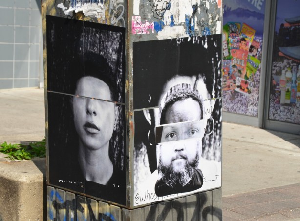 large black and white faces on grey metal box on sidewalk, one side has person with eyes missing and the other side is a face made of a composite of at least three different faces 