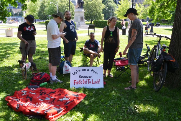 a group of people on the grass at Queens Park, with a sign that says we are having a picnic because Doug Ford is out to lunch 