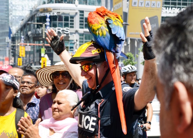 a police man holds a brightly coloured parrot, or rather the parrot sits on his bike helmet 