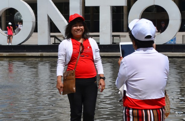 one woman takes another woman's photo with an ipad in front of the Toronto 3 D sign 