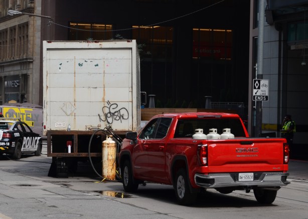 part of a film set on Adelaide, a red pick up truck with propane tanks in the back, with another tank wired to the back of a white panel truck