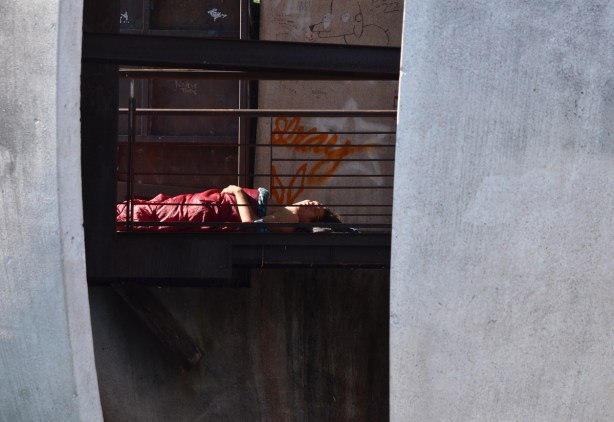 a person is asleep, on back, under a maroon sleeping bag, inside a spherical art installation with a slit in it that lets in light such that sleeper is spotlit