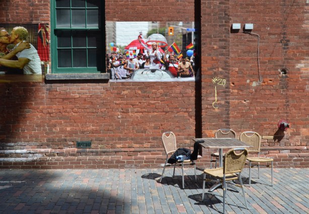 pictures on a brick wall, above a table with empty chairs, outdoors, 