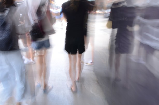blurry picture of peoples' legs and feet and shoes as they walk on a sidewalk