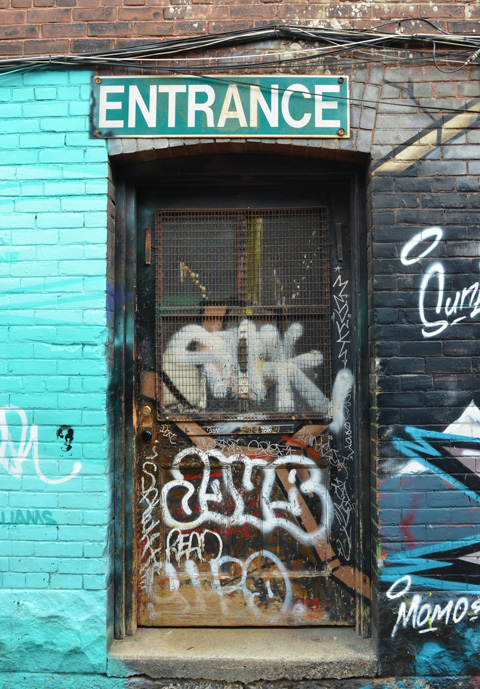old dark door with entrance sign over the top, with lots of graffiti on the door, mural painted on walls beside the door 
