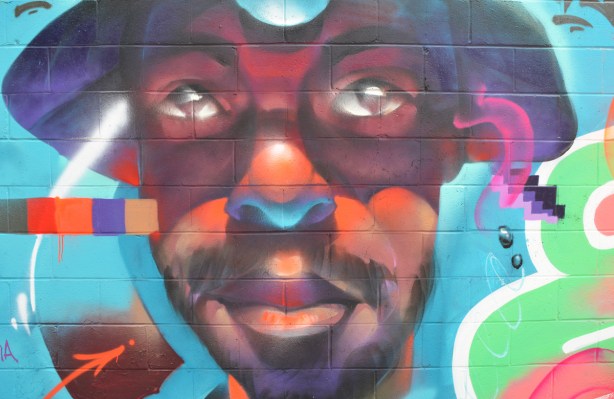 portrait of a man in shades of brown, orange and purple, with a hat, by luvsomone, a mural in an alley