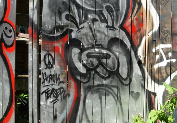a black on silver poser bunny painting on a wood fence in an alley, a little happy face is in the top left corner of the picture 
