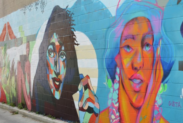 two large faces painted side by side in an alley 