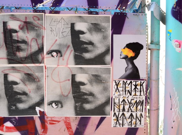 six paper paste up graffiti pieces, four with mens faces in profile with top of head missing but eye beside the chin, one with black woman in profile with yellow over her face, and one with words and symbols