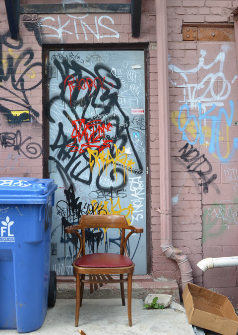 pale blue door with graffiti on it, a blue rubbish bin and chair in front of the door 