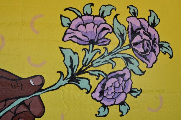 a dark brown hand holding a sprig of small light purple flowers