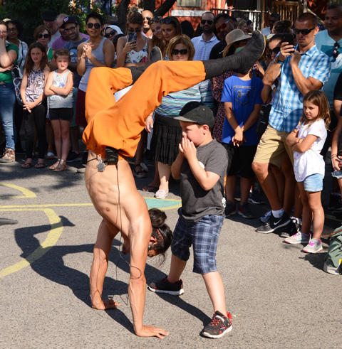 hiro son, a Japanese performance artist is standing on his hands in front of a young boy who has his hands close to his mouth, crowd watching in the background 