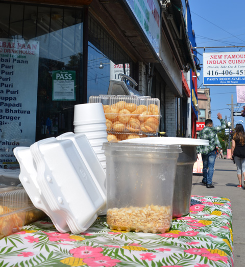food and containers on a table outside a store, with pink and green floral table cloth