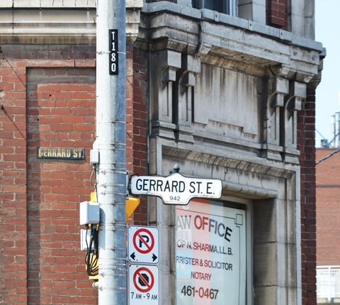 side of an old brick building with stone features, an old street sign on the building Gerrard Street, now a law office with signs in the windows