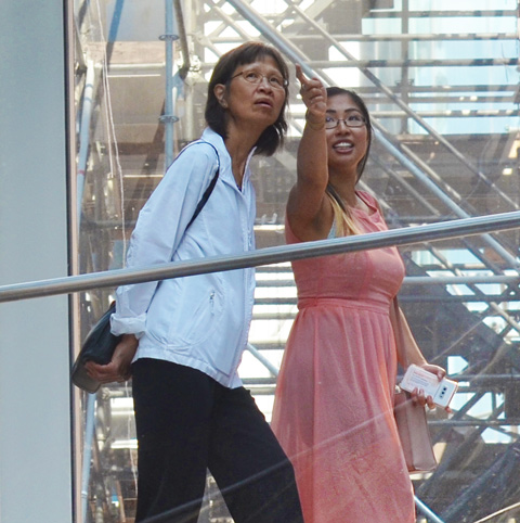two women walking across the passage from the Eaton Centre to the Bay, over Queen Street. One is wearing a pink dress and is pointing to something. the other woman is trying to figure out what she is pointing at 