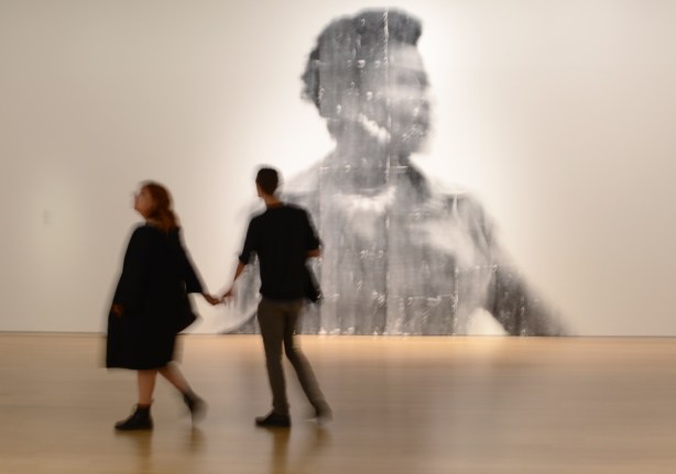 a couple holding hands with the woman leading the man, out of focus, walking past a large out of focus picture of a woman, a photo by Sandra Brewster as part of her blur series