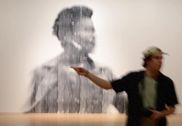people, out of focus, walking past a large out of focus picture of a woman, a photo by Sandra Brewster as part of her blur series, a man pointing