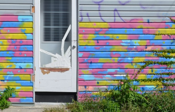 door with glass panel with white tape over one of the bottom corners, walls painted in yellow, pink, and blue splotches