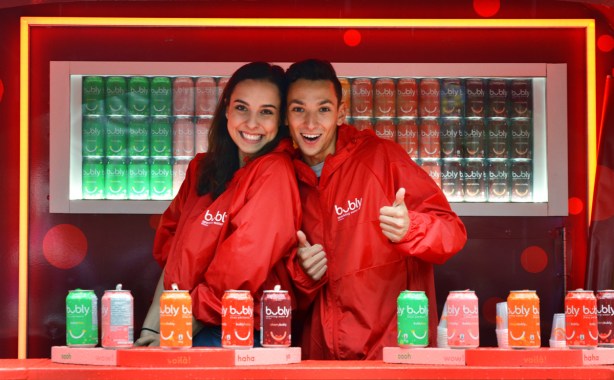 two young people working in a red booth for bubly drinks, both smiling and one is giving a thumbs up