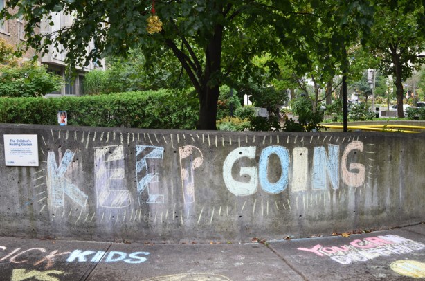 chalk writing on a low concrete wall in a small park that says keep going 