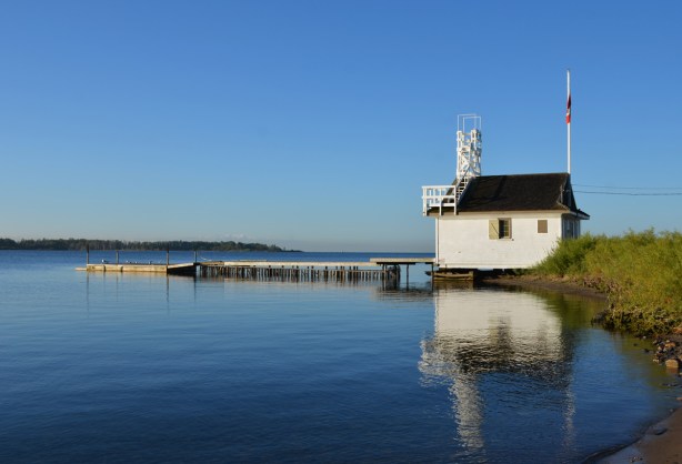 cherry lifeguard station, with dock in front, very calm and still water, reflections of the building in the water, early morning, 