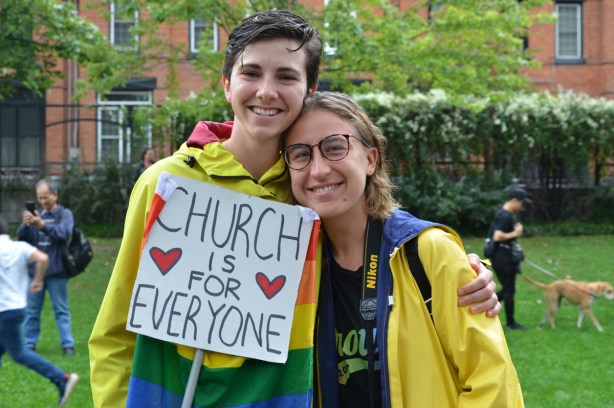 two women in yellow rain jackets holding a sign that says Church is for everyone 