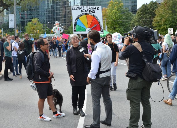 a woman is being interviewed for television, at a climate change protest,