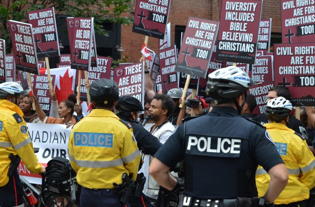 David Lynn talks to his protesters, with signs and placards, behind a police line 