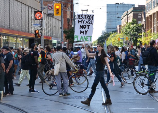 cyclists line Bay street at College street while they wait for a break in the climate strike march, one woman holds a sign that says destroy my ass not my planet