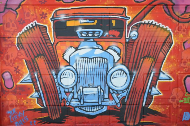 a fun mural of an old car by dudeman, in reds and oranges with front grille and radiator in blues